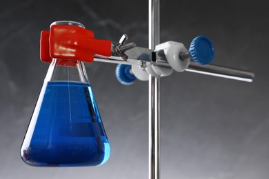 Retort stand and laboratory flask with liquid on grey background, closeup