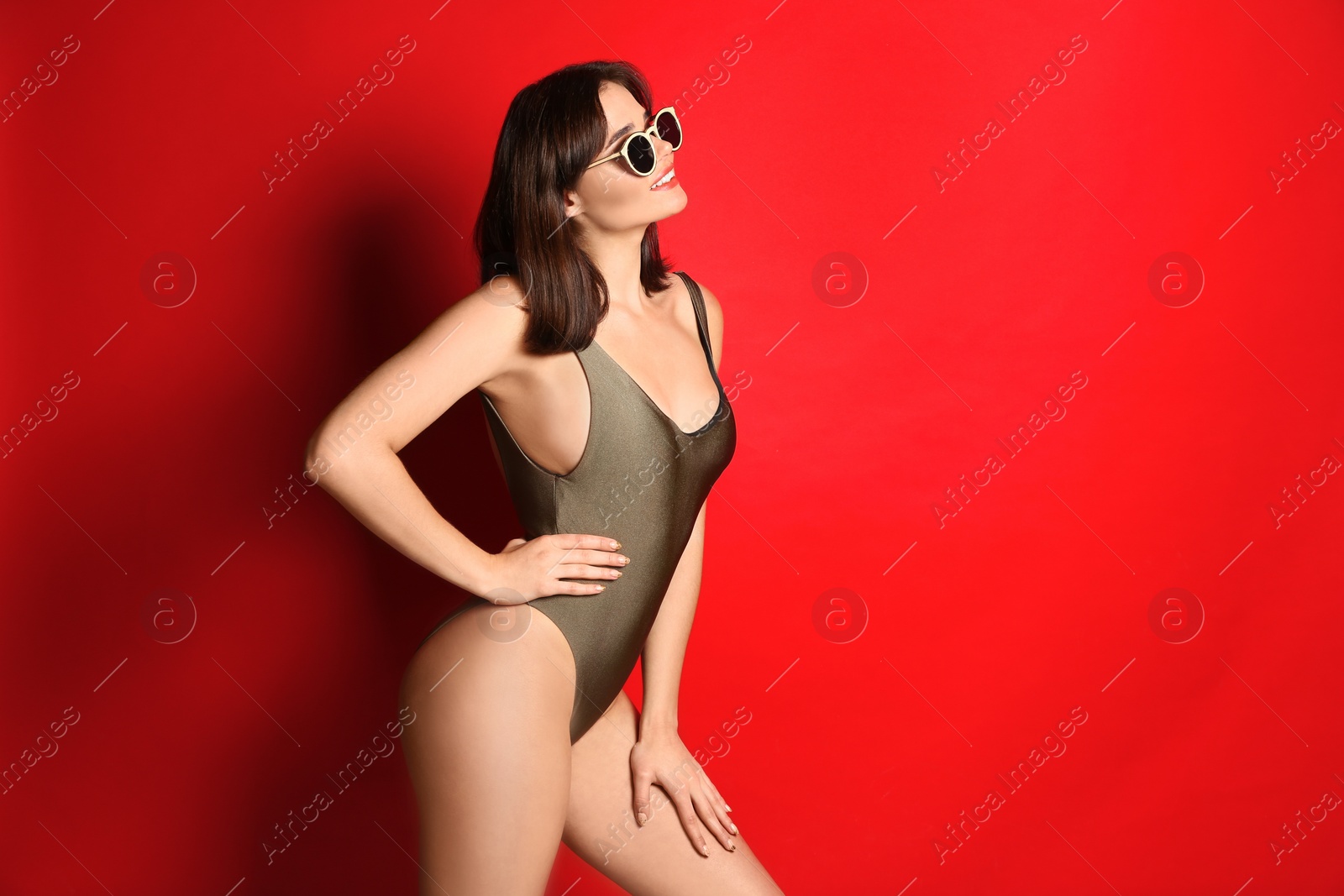 Photo of Beautiful woman in stylish swimsuit and sunglasses on red background. Space for text