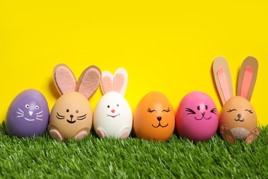 Photo of Several eggs as Easter bunnies among others on green grass against yellow background