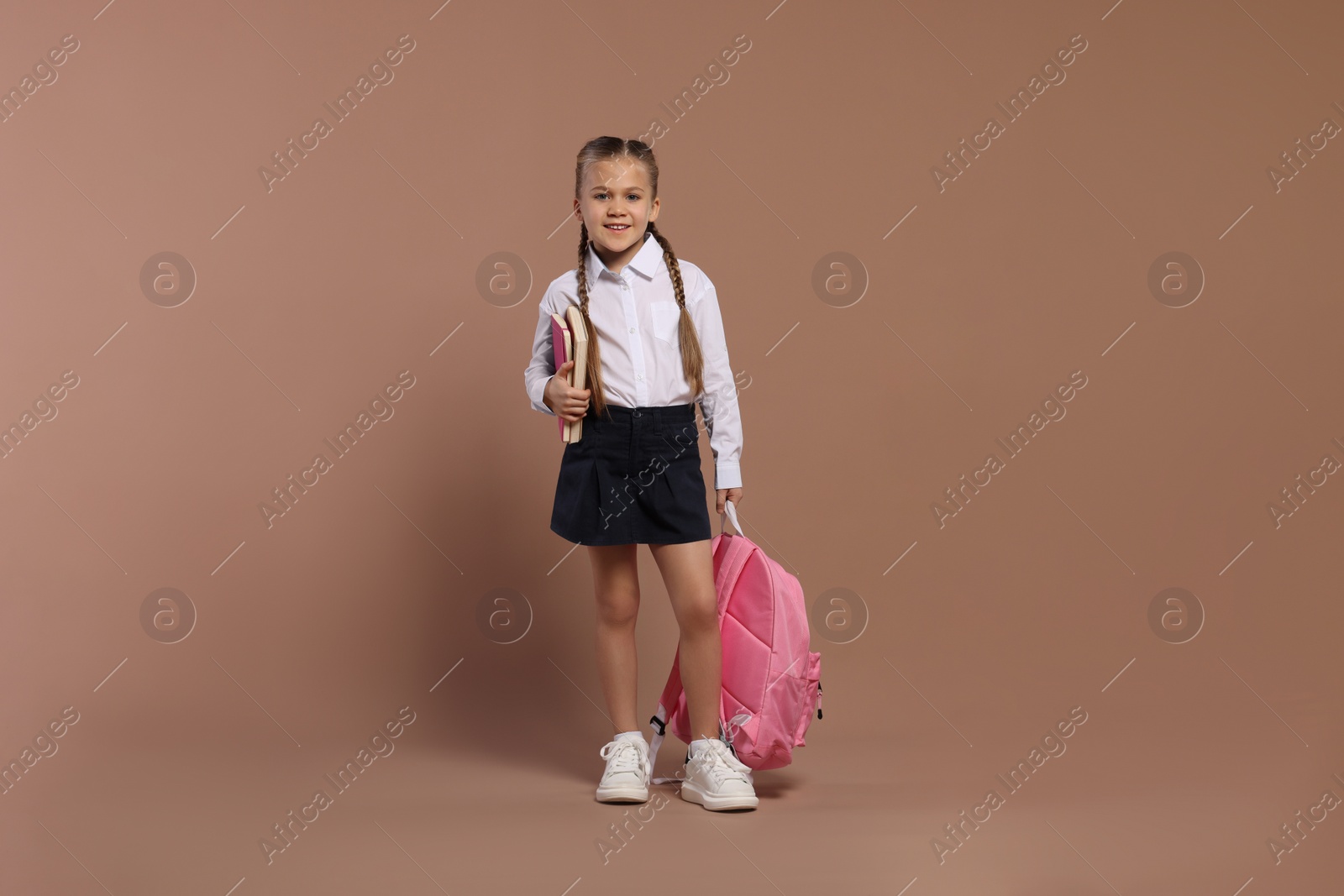 Photo of Happy schoolgirl with backpack and books on brown background