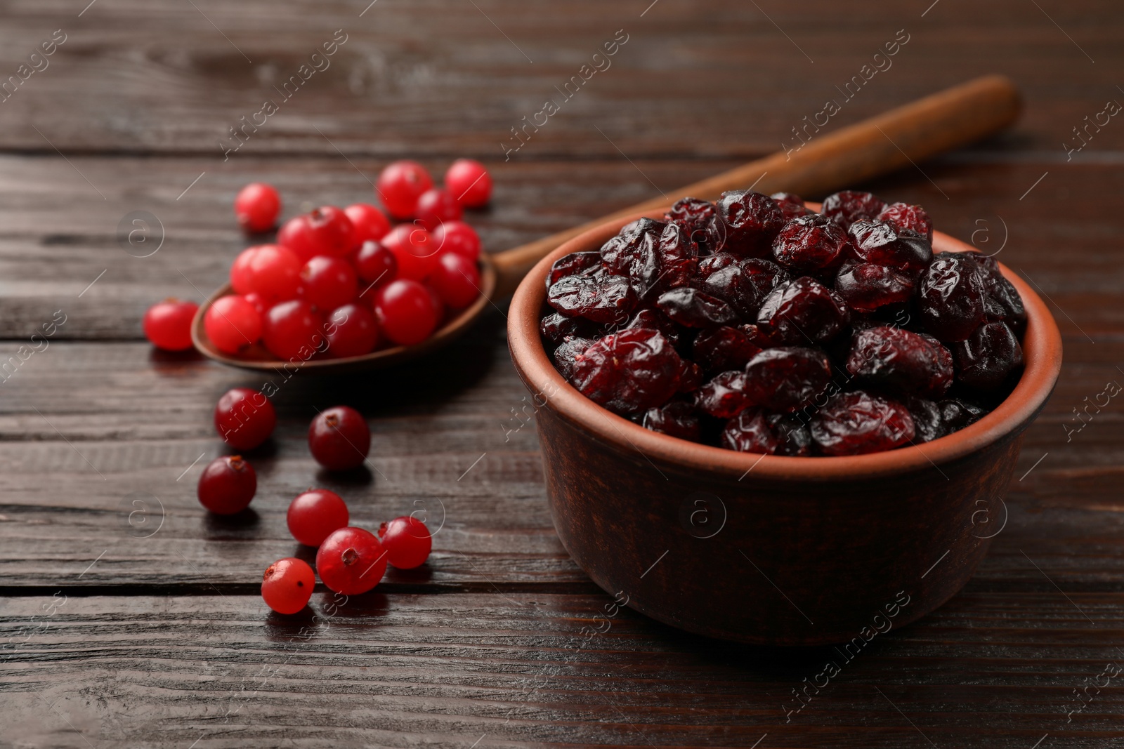 Photo of Tasty dried cranberries in bowl and fresh ones on wooden table, closeup