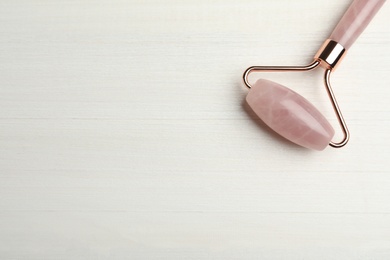 Natural rose quartz face roller on white wooden background, top view. Space for text