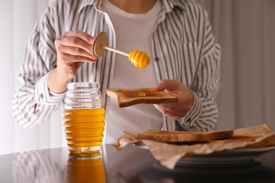 Photo of Woman pouring honey onto toast at black table, closeup