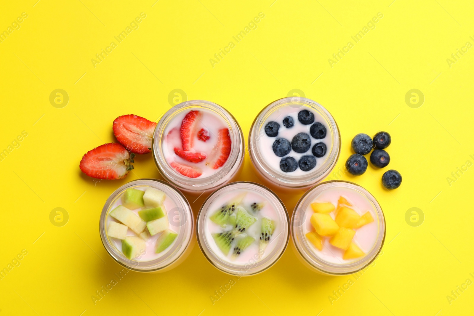 Photo of Tasty yogurt in glass jars and ingredients on yellow background, flat lay