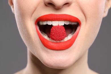 Photo of Young woman with beautiful red lips makeup eating candy on grey background, closeup