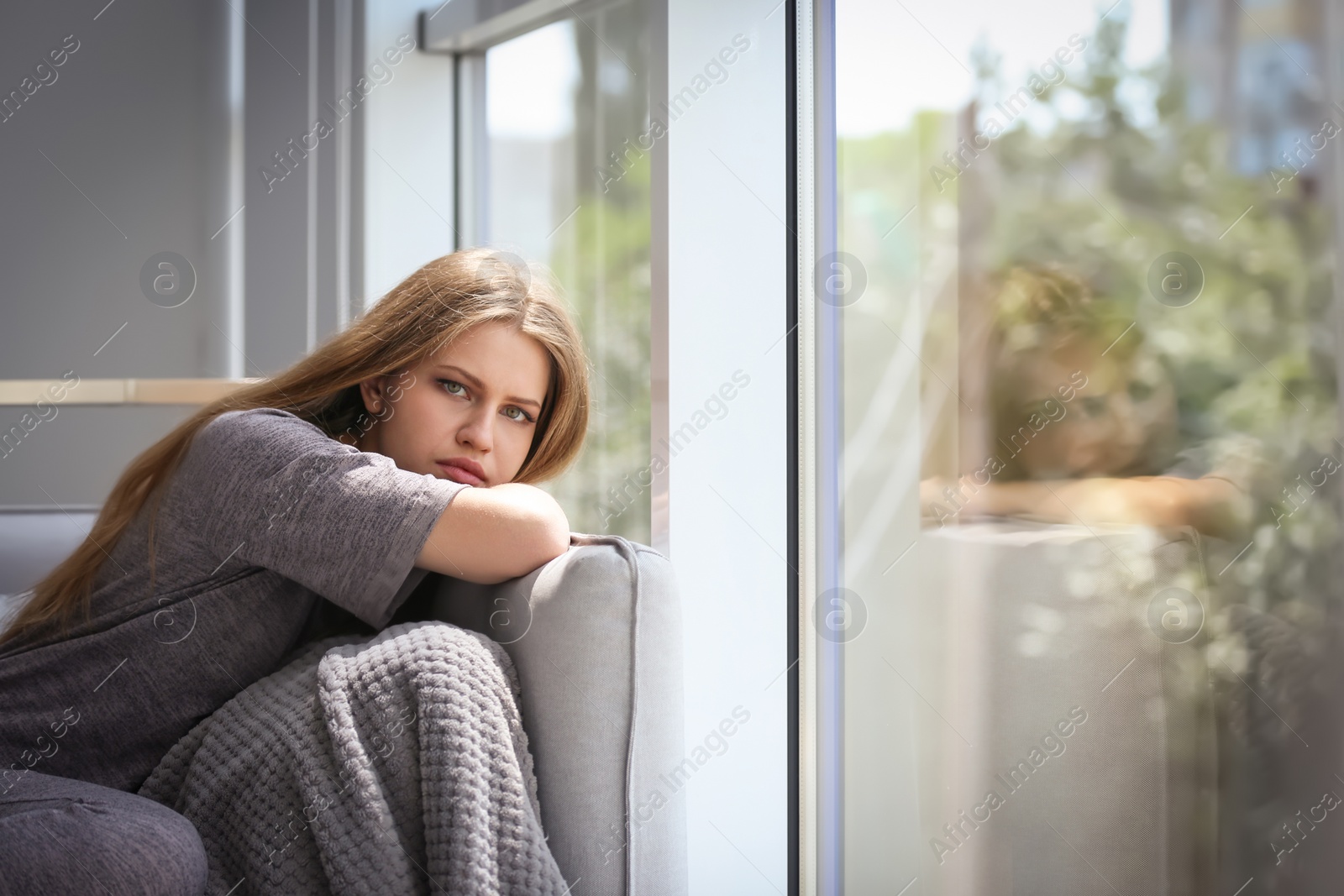 Photo of Depressed young woman sitting on sofa at home