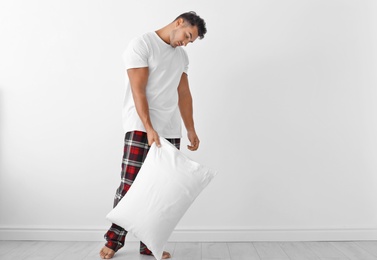 Photo of Sleepy young man with soft pillow near white wall