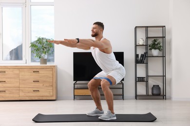 Photo of Athletic man doing exercise with elastic resistance band on mat at home
