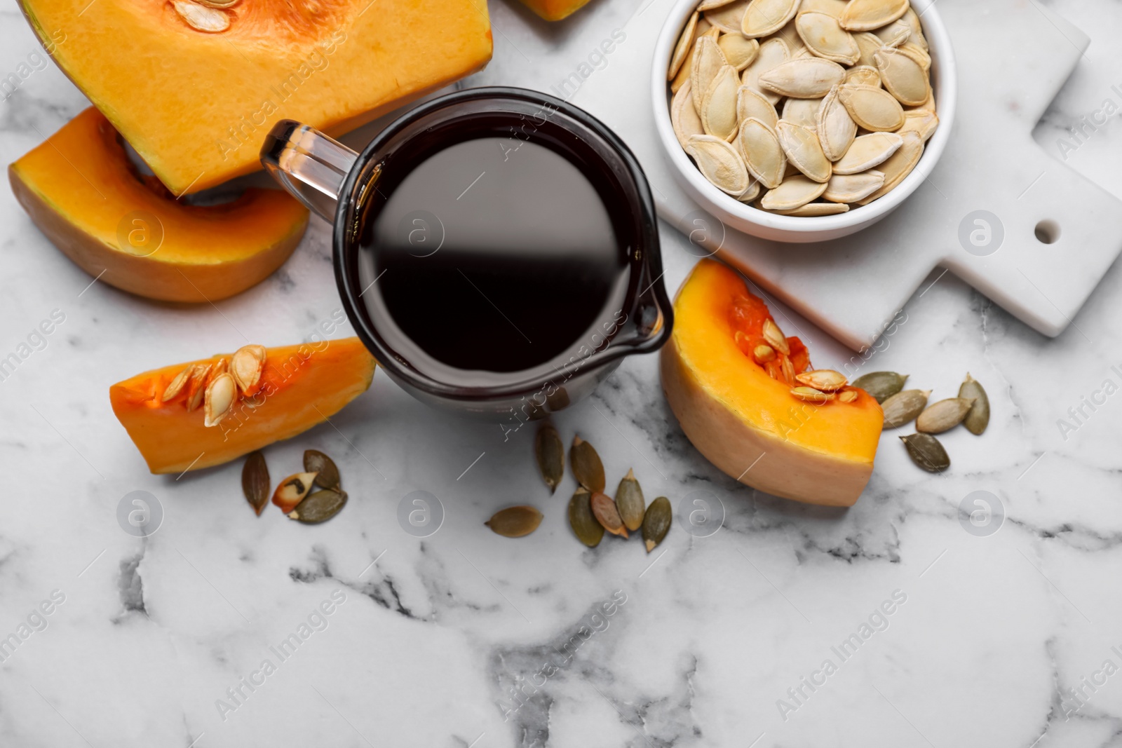 Photo of Flat lay composition with fresh pumpkin seed oil in glass pitcher on white marble table. Space for text