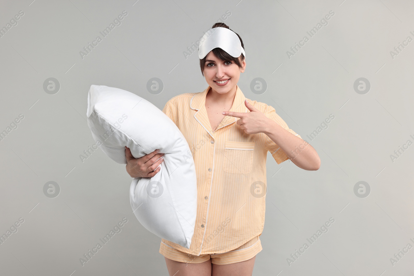 Photo of Happy woman in pyjama and sleep mask holding pillow on grey background