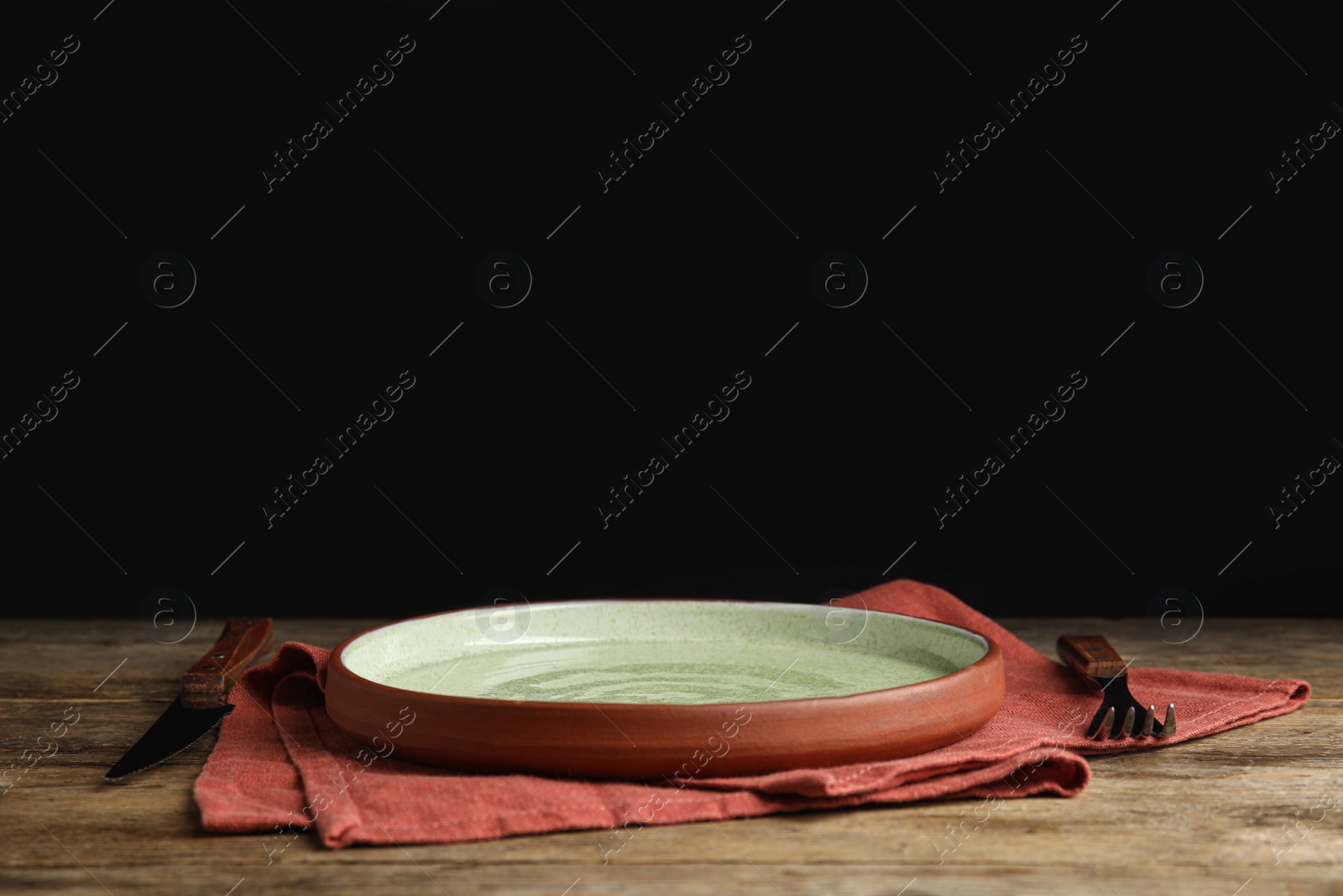 Photo of Empty plate, cutlery and napkin on wooden table against black background. Space for text