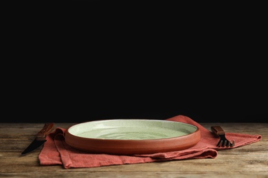 Photo of Empty plate, cutlery and napkin on wooden table against black background. Space for text