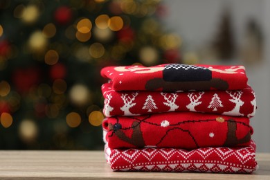 Photo of Stack of different Christmas sweaters on table against blurred lights, space for text