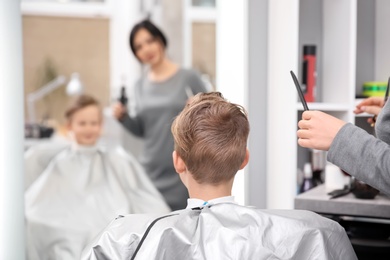 Professional female hairdresser working with little boy in salon