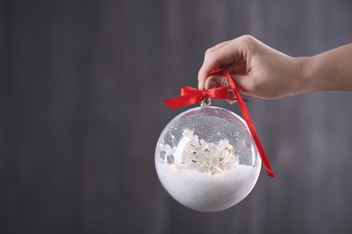 Woman holding decorative snow globe on grey background, closeup. Space for text