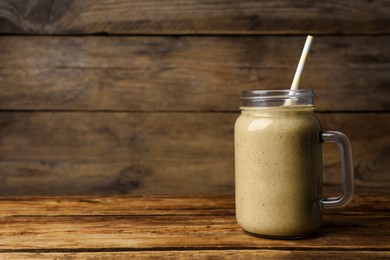 Photo of Mason jar with delicious fruit smoothie on wooden table. Space for text