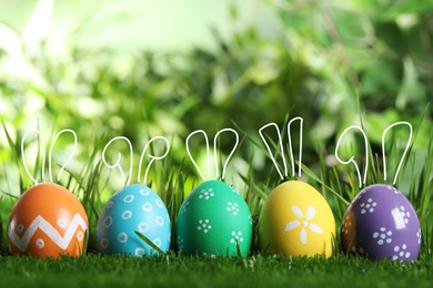 Image of Bright Easter eggs with cute bunny ears in green grass