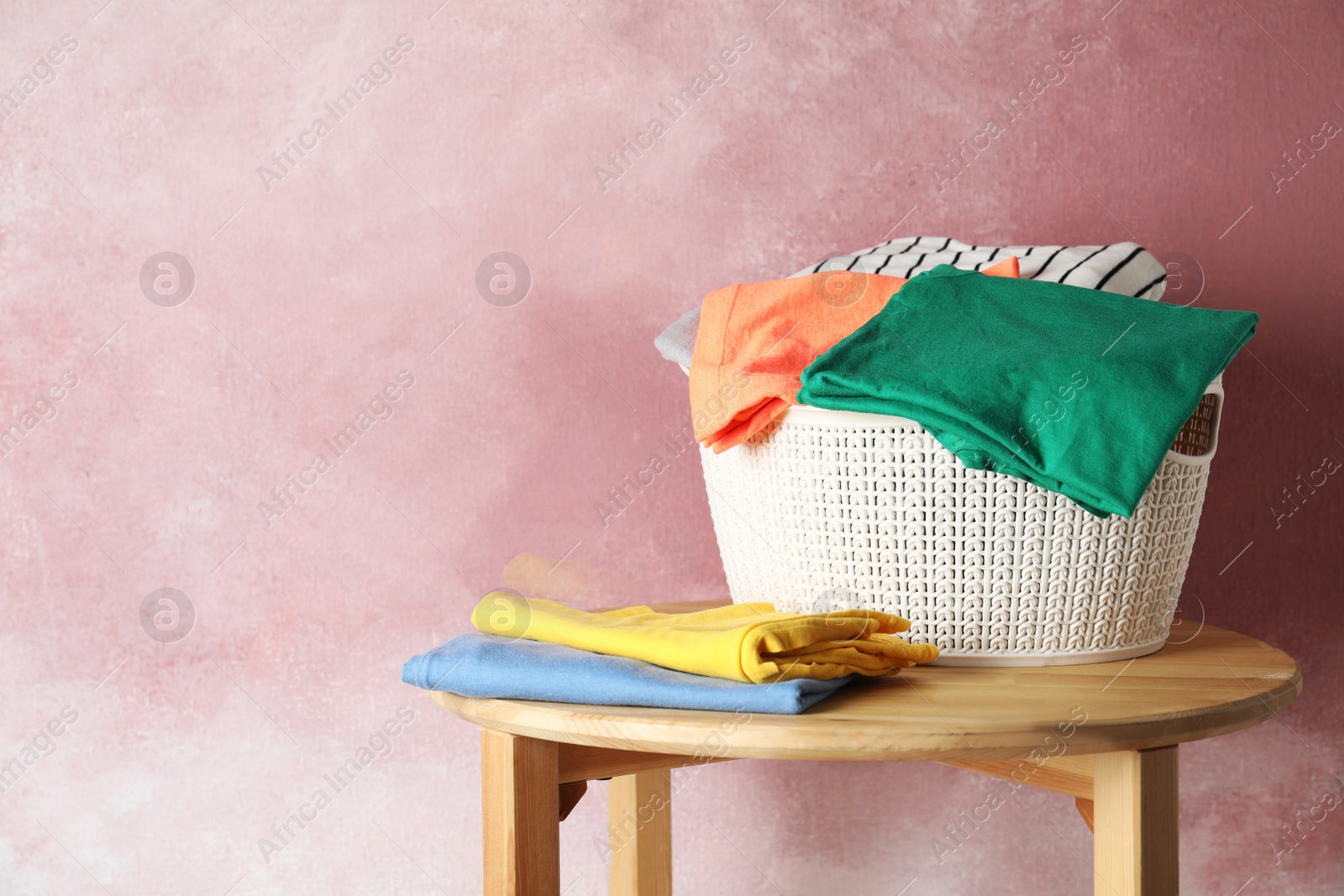 Photo of Basket with clean laundry on wooden table near pink wall, space for text