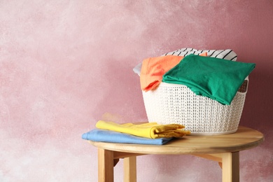 Basket with clean laundry on wooden table near pink wall, space for text