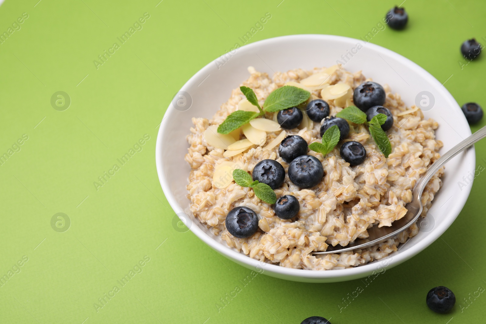 Photo of Tasty oatmeal with blueberries, mint and almond petals in bowl on light green background. Space for text