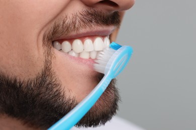 Photo of Man brushing his teeth with plastic toothbrush on light grey background, closeup. Space for text