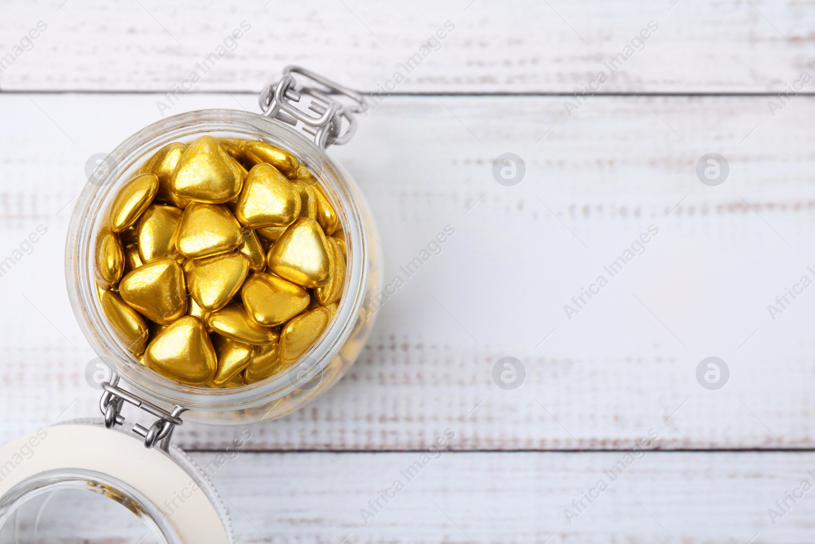 Photo of Jar with delicious heart shaped candies on white wooden table, top view. Space for text