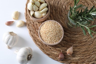 Photo of Dehydrated garlic granules in bowl, rosemary and fresh cloves on white table, flat lay