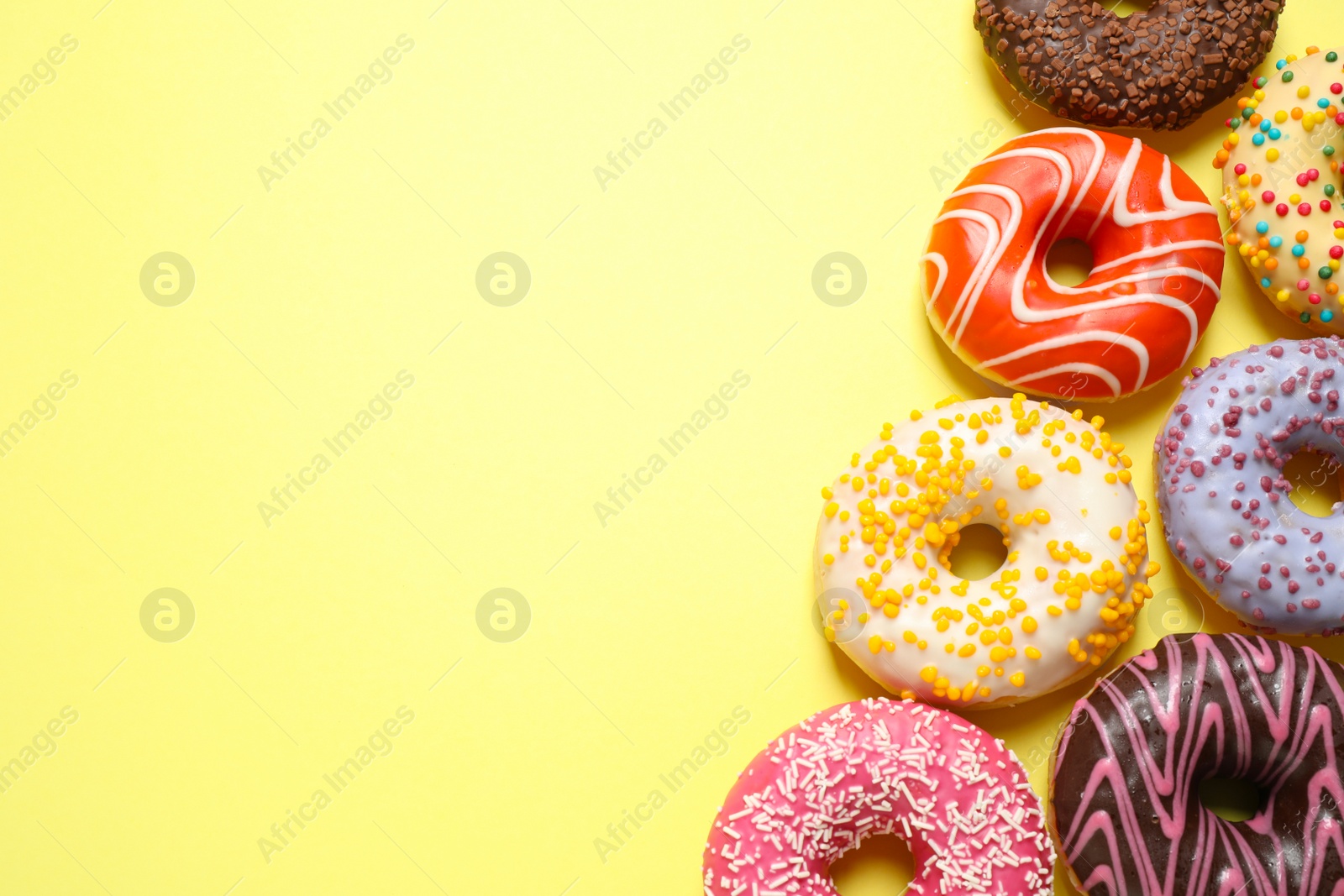 Photo of Delicious glazed donuts on yellow background, flat lay. Space for text