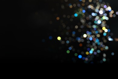 Blurred view of colorful festive lights on black background, space for text. Bokeh effect