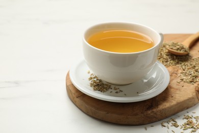 Photo of Fennel tea in cup and seeds on white marble table, closeup. Space for text