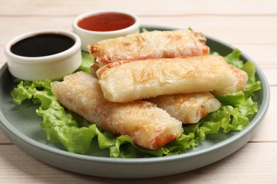 Photo of Delicious fried spring rolls and sauces on light wooden table, closeup