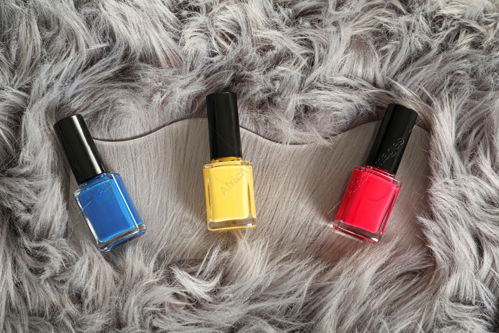 Photo of Bright nail polishes in bottles on grey faux fur, top view