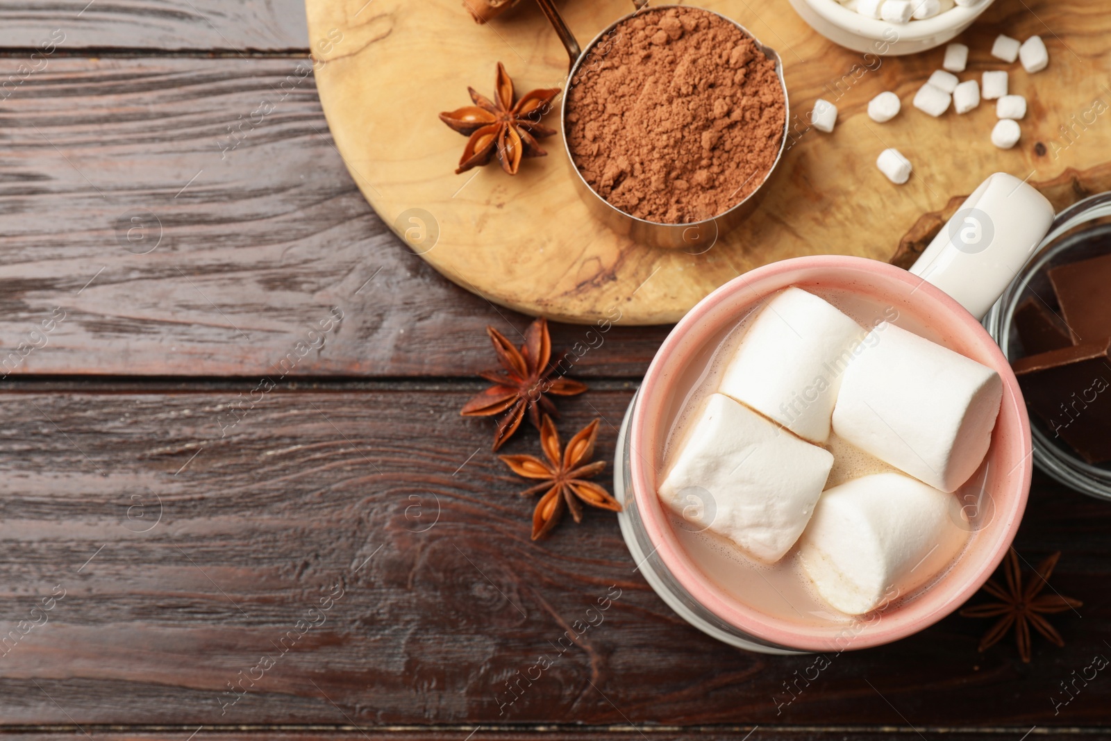 Photo of Tasty hot chocolate with marshmallows and ingredients on wooden table, flat lay. Space for text