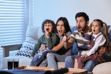 Photo of Surprised family watching TV with pizza on sofa at home