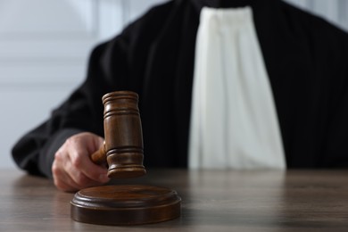 Judge with gavel sitting at wooden table indoors, closeup