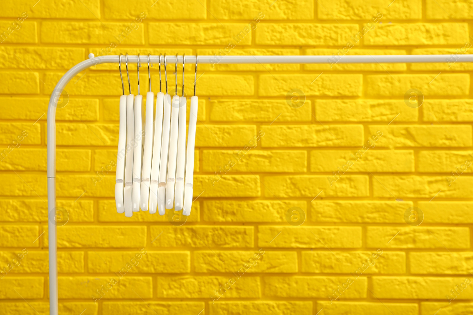 Photo of Wardrobe rack with many hangers near yellow brick wall