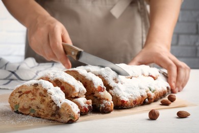 Photo of Woman cutting traditional Christmas Stollen with icing sugar at white wooden table, closeup