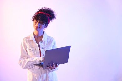 Photo of Beautiful young woman with laptop on color background in neon lights. Space for text