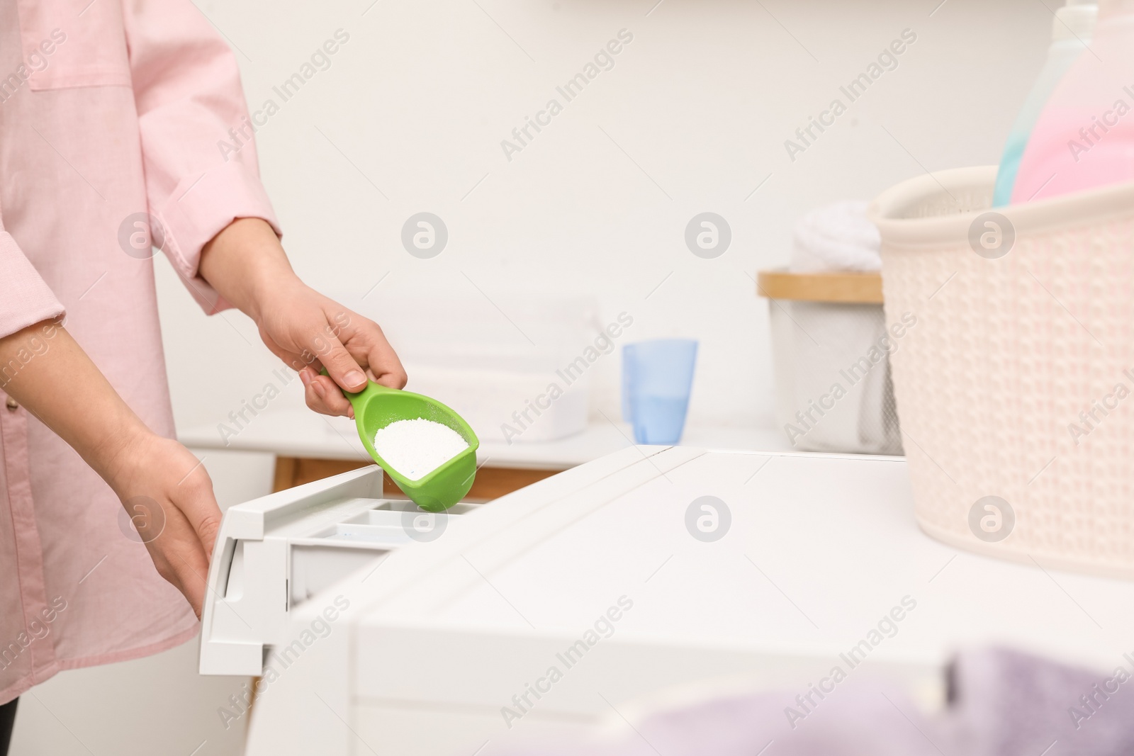 Photo of Woman pouring powder into drawer of washing machine in laundry room, closeup