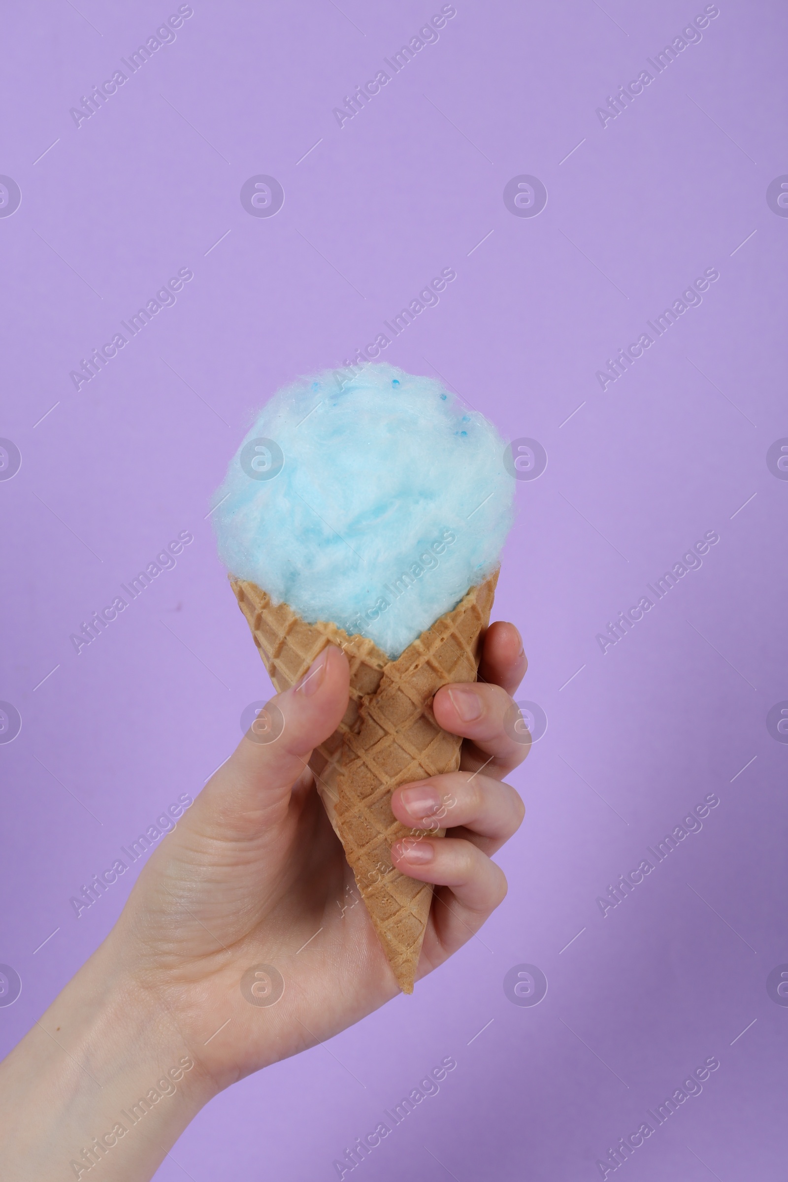 Photo of Woman holding waffle cone with cotton candy on violet background, closeup