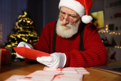 Photo of Santa Claus opening letter at his workplace in room decorated for Christmas