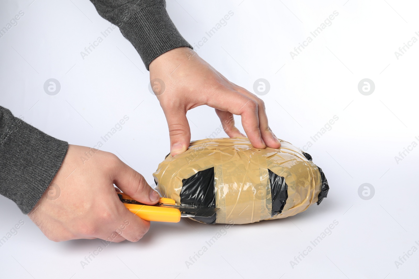 Photo of Smuggling and drug trafficking. Man opening package of narcotics with box cutter on white background, closeup