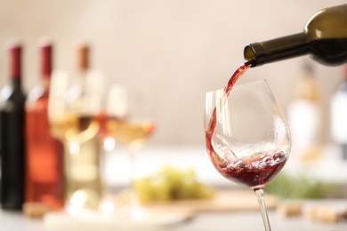 Pouring red wine from bottle into glass on blurred background. Space for text