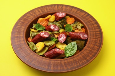 Delicious sausage and baked vegetables on yellow background, closeup