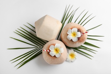 Photo of Fresh coconuts with drinking straws and flowers on white background, flat lay