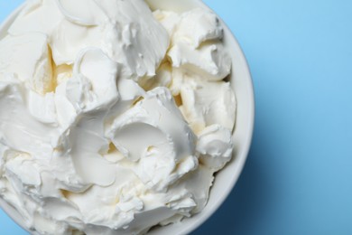 Photo of Bowl of tasty cream cheese on light blue background, top view