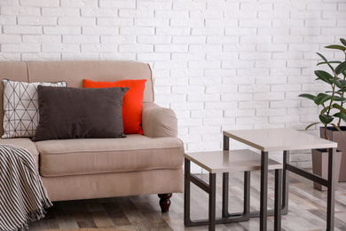 Photo of Soft pillows on sofa near white brick wall at home