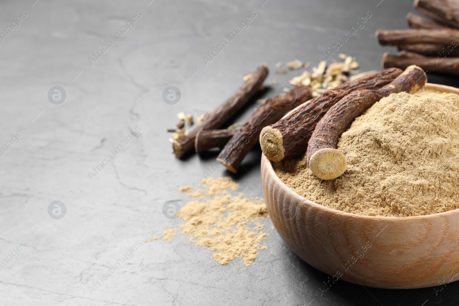 Photo of Powder in bowl and dried sticks of liquorice root on black table, space for text