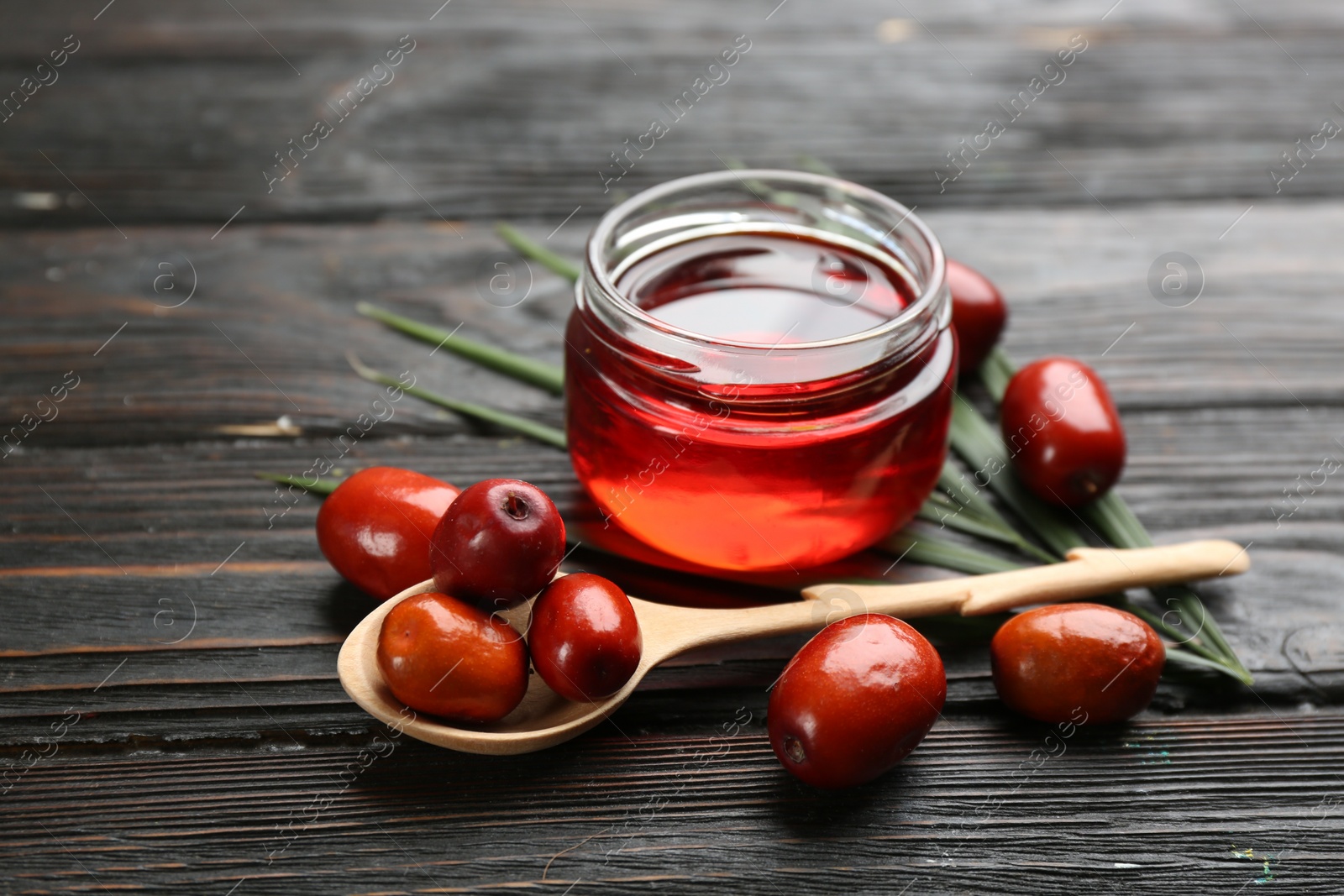 Photo of Palm oil in glass jar, tropical leaf and fruits on wooden table