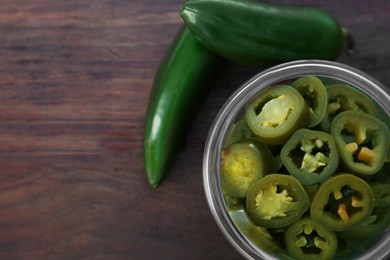 Photo of Fresh and pickled green jalapeno peppers on wooden table, flat lay. Space for text